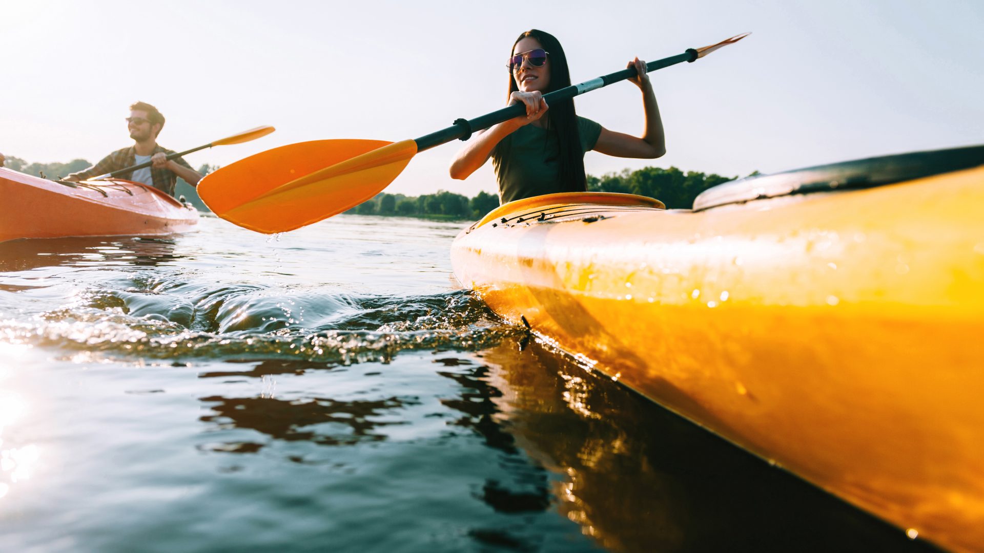 two people kayaking on the water with a sun in the background at The Sawmill Park